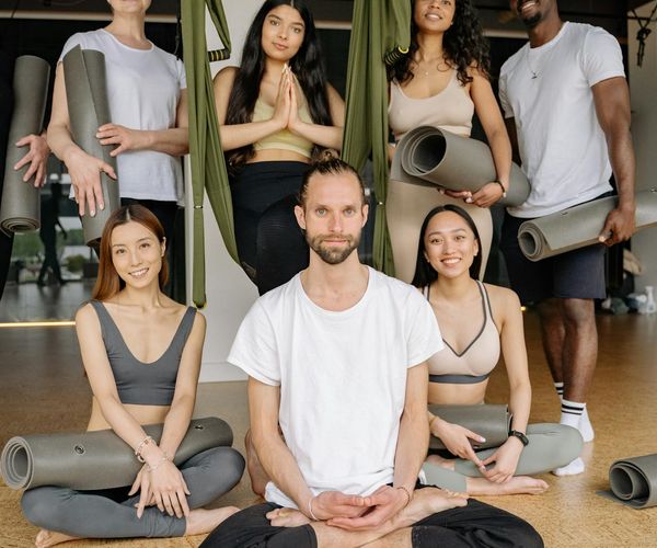 Diverse group of people smiling and preparing for a yoga class in a bright studio.